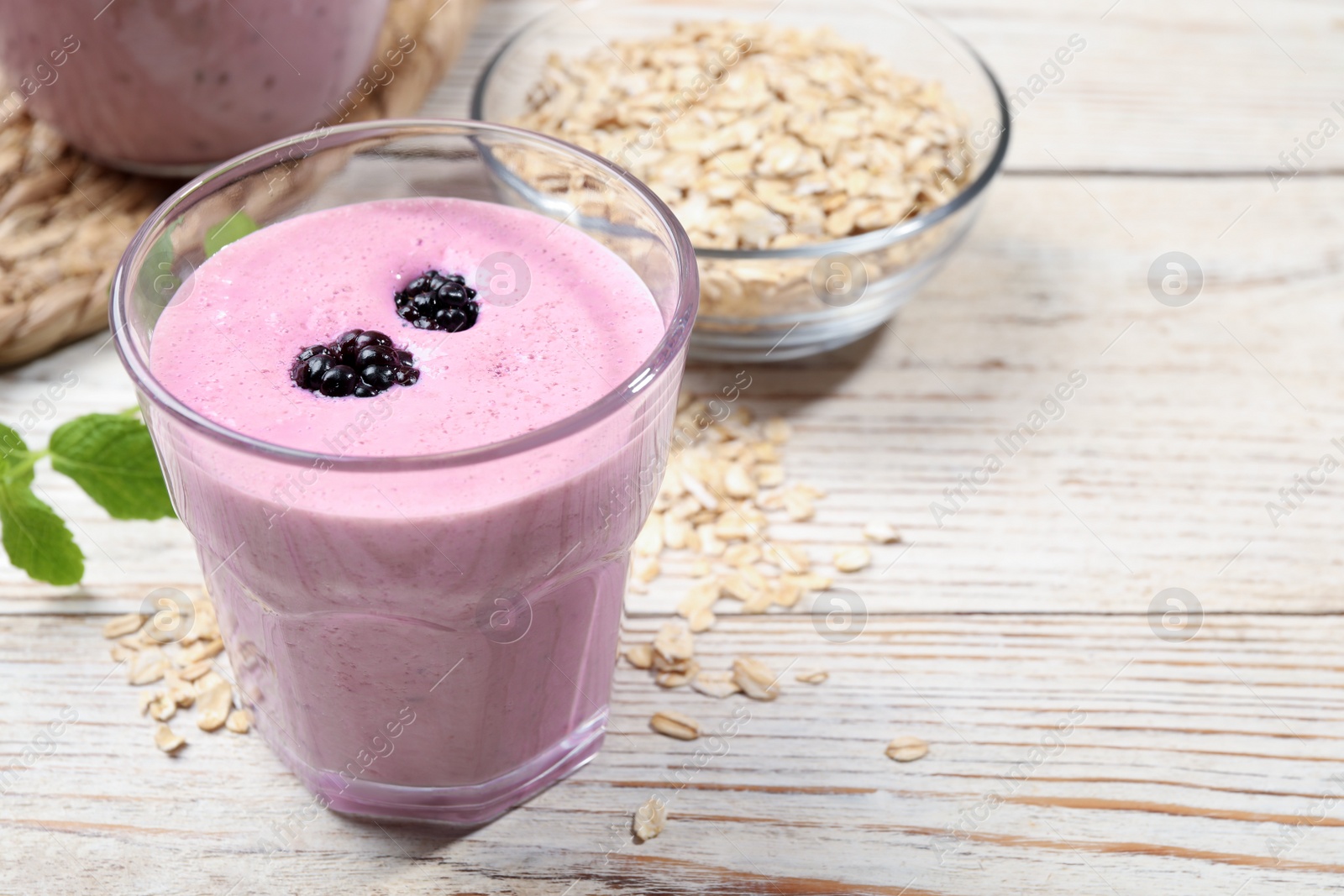 Photo of Glass of blackberry smoothie and oatmeal on light wooden table, closeup. Space for text