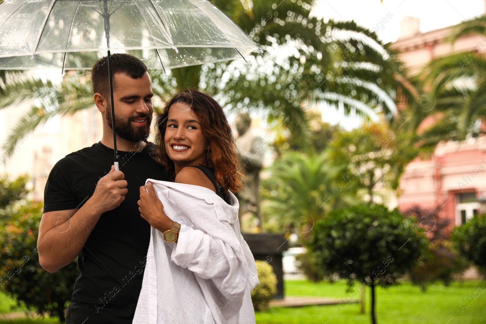 Photo of Young couple with umbrella enjoying time together under rain on city street, space for text