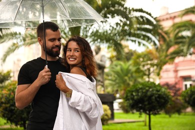 Young couple with umbrella enjoying time together under rain on city street, space for text