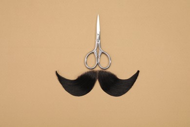 Artificial moustache and scissors on beige background, top view