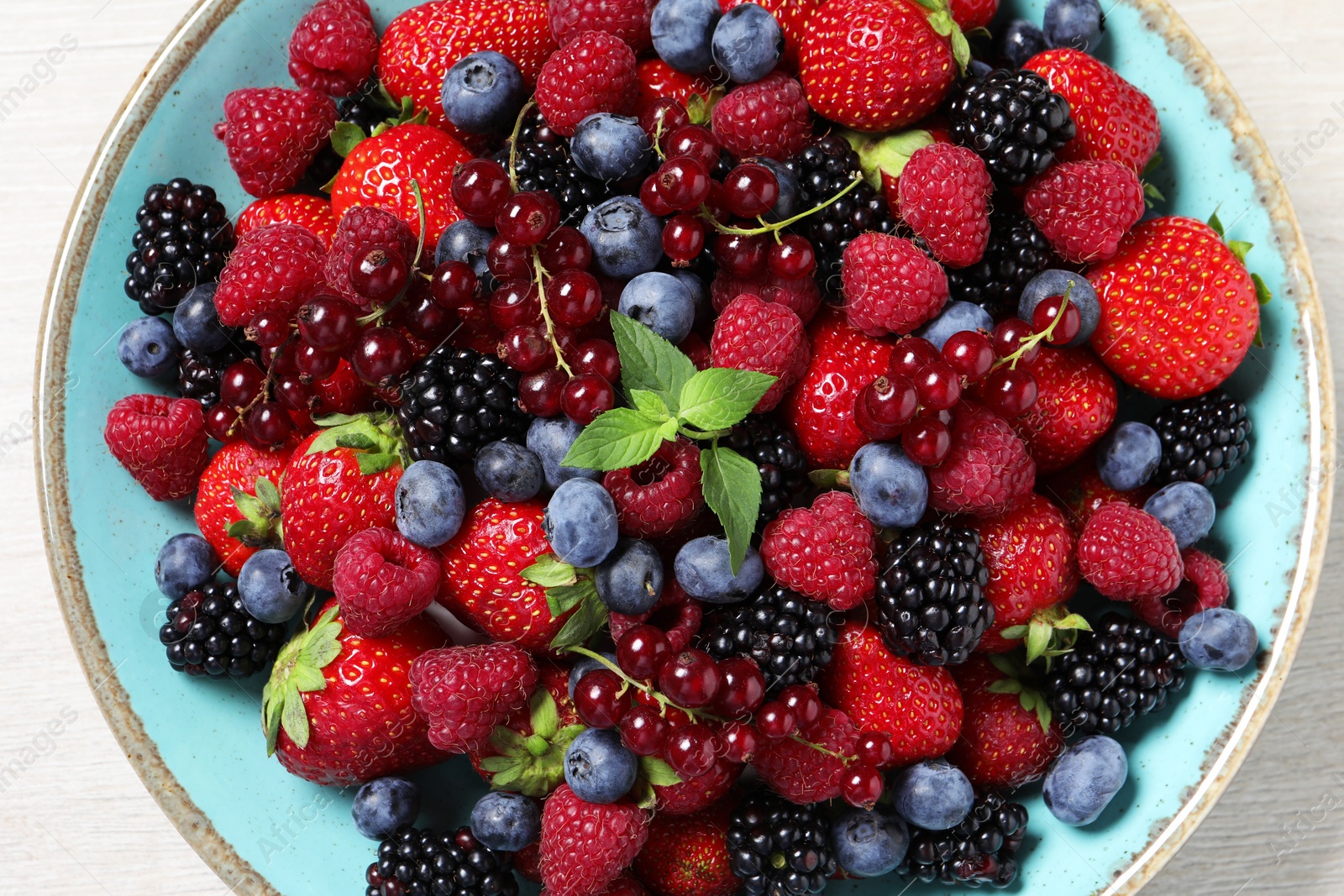 Photo of Many different fresh ripe berries in bowl on white wooden table, top view