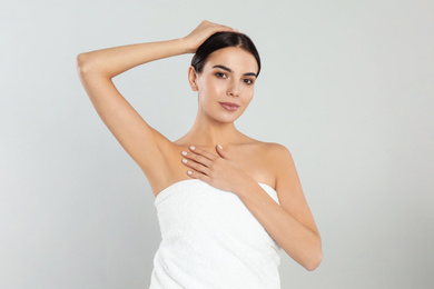 Young woman showing hairless armpit after epilation procedure on light grey background