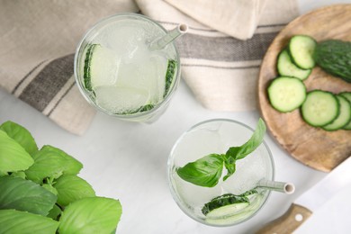 Tasty fresh cucumber water with basil on white table, flat lay