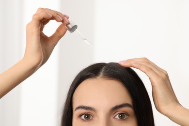 Woman applying hair serum in room, closeup. Cosmetic product