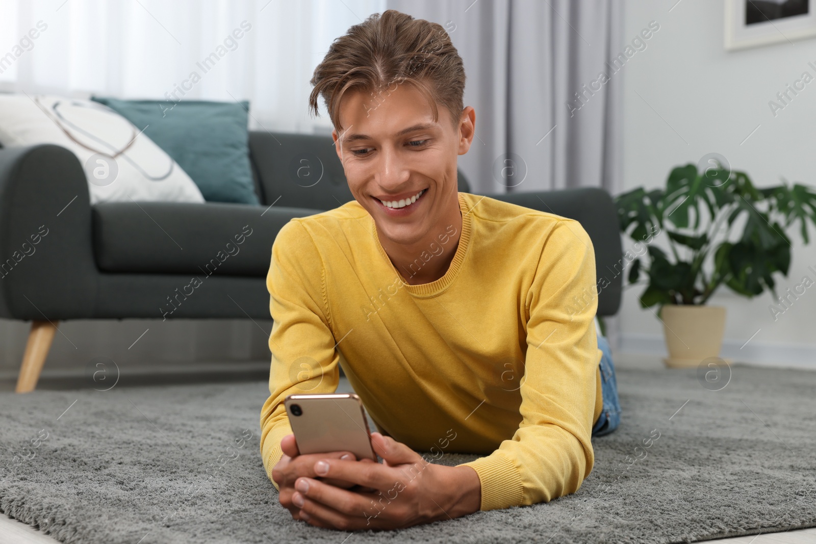 Photo of Happy young man having video chat via smartphone on carpet indoors