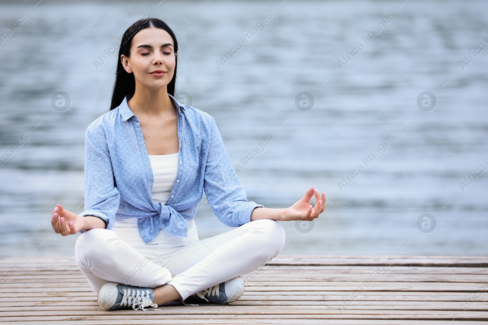 Photo of Young woman meditating near river. Space for text