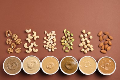Photo of Many tasty nut butters in bowls and nuts on brown table, flat lay. Space for text
