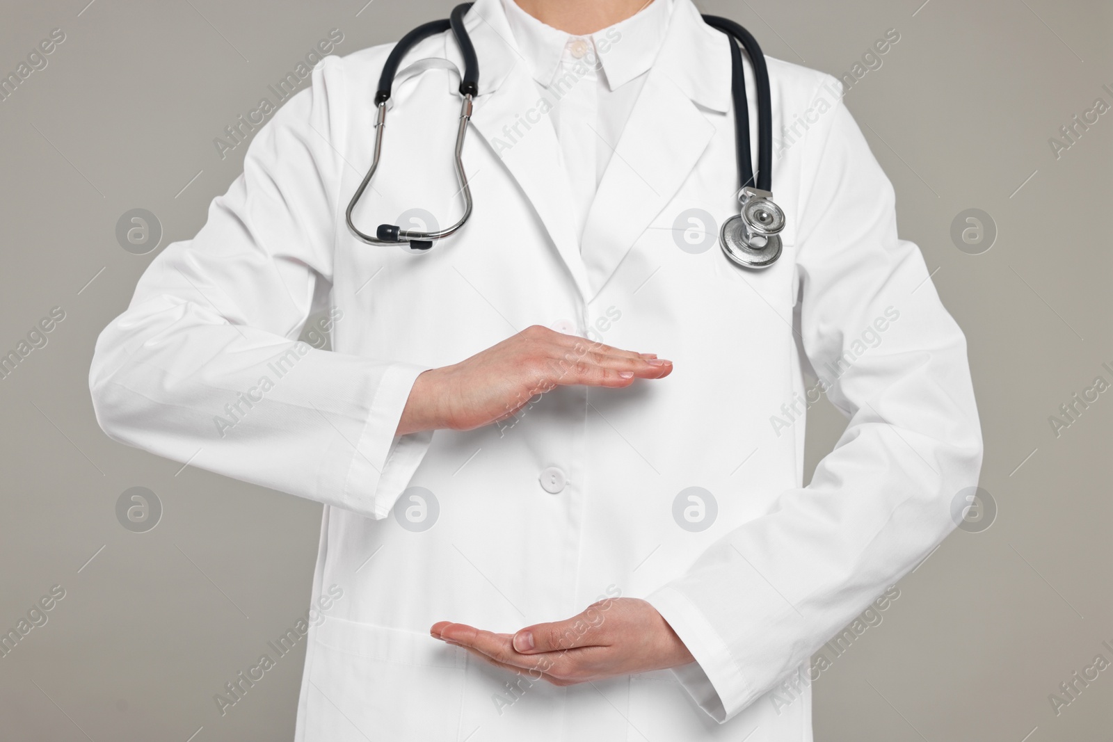 Photo of Doctor with stethoscope holding something on grey background, closeup