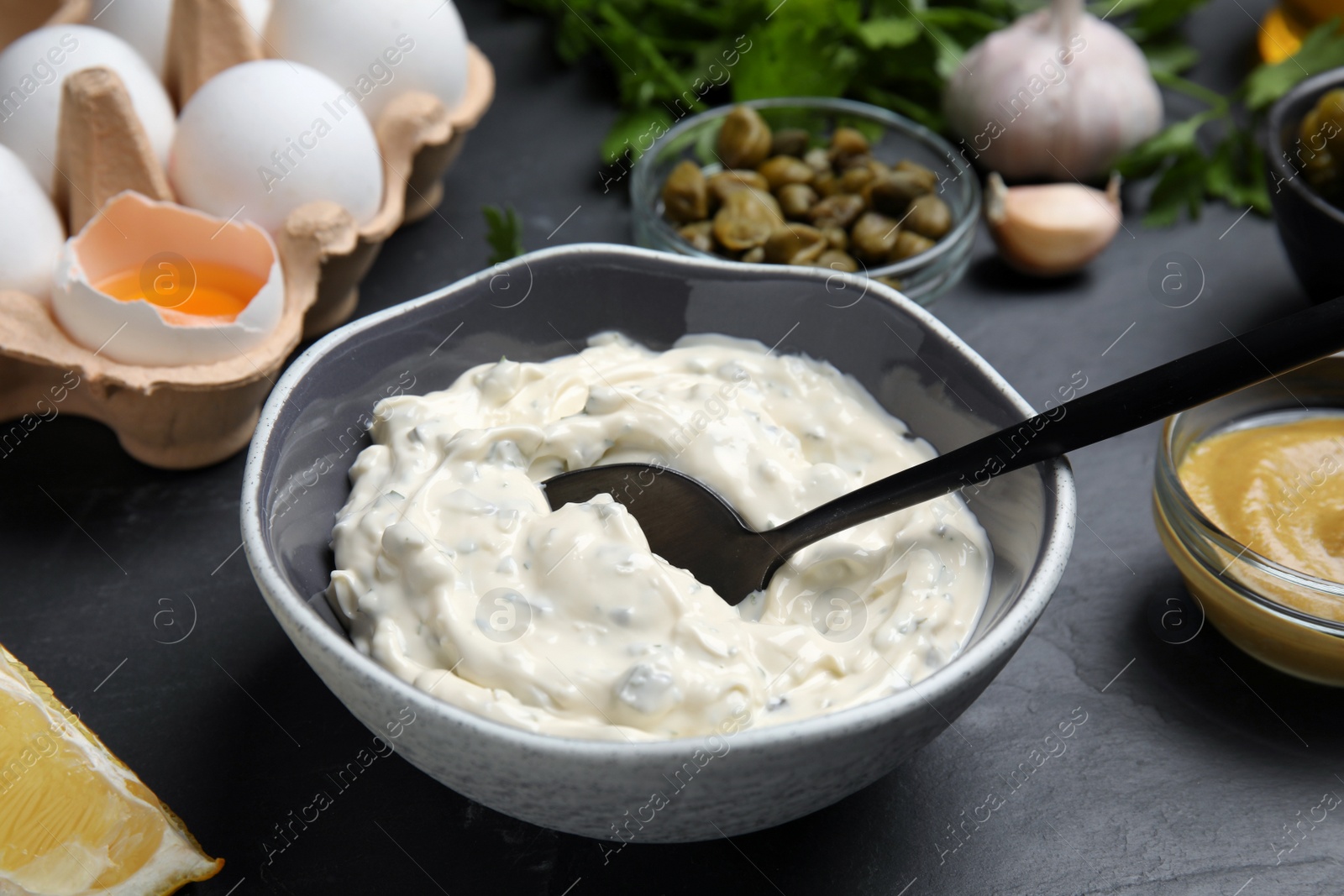 Photo of Tasty tartar sauce and ingredients on black table