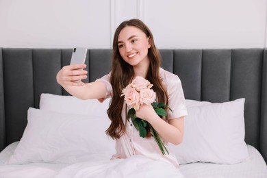 Photo of Beautiful young woman taking selfie with rose flowers on bed in room