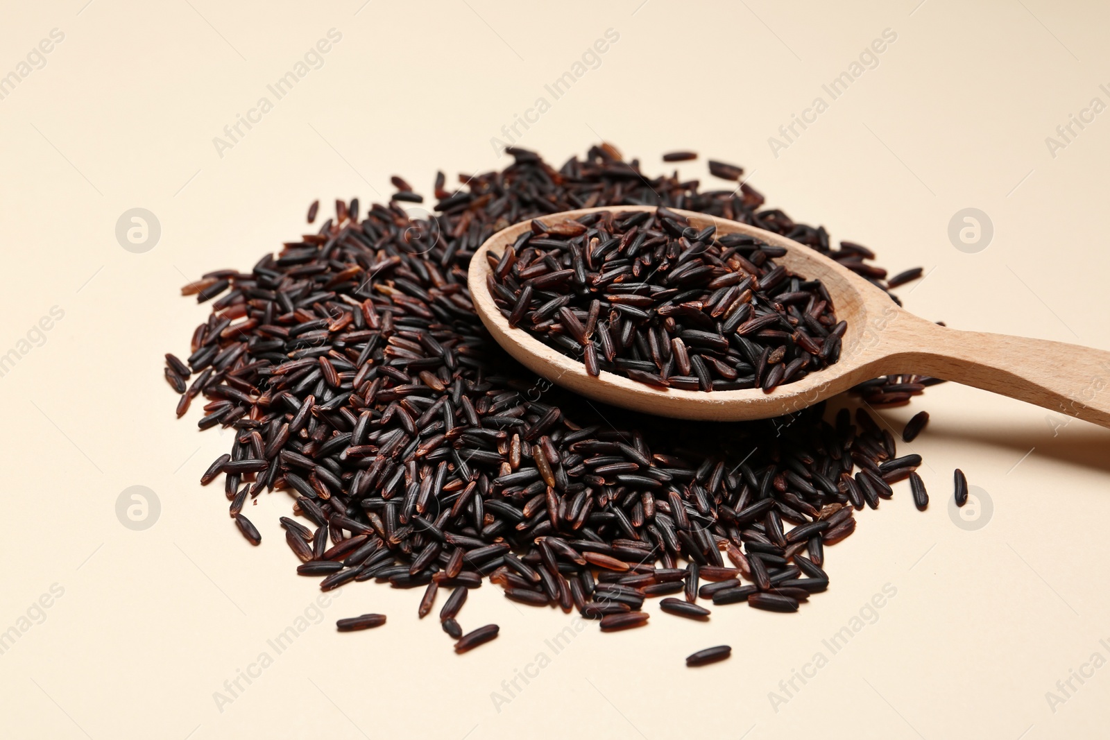 Photo of Black rice and wooden spoon on color background