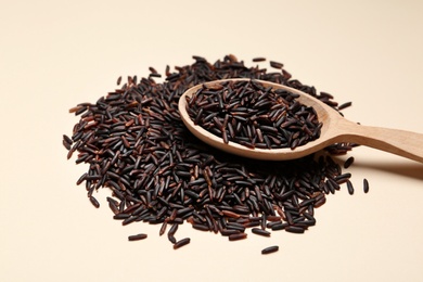 Black rice and wooden spoon on color background