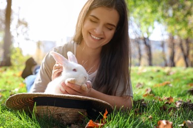 Photo of Happy woman with cute white rabbit in park, focus on pet