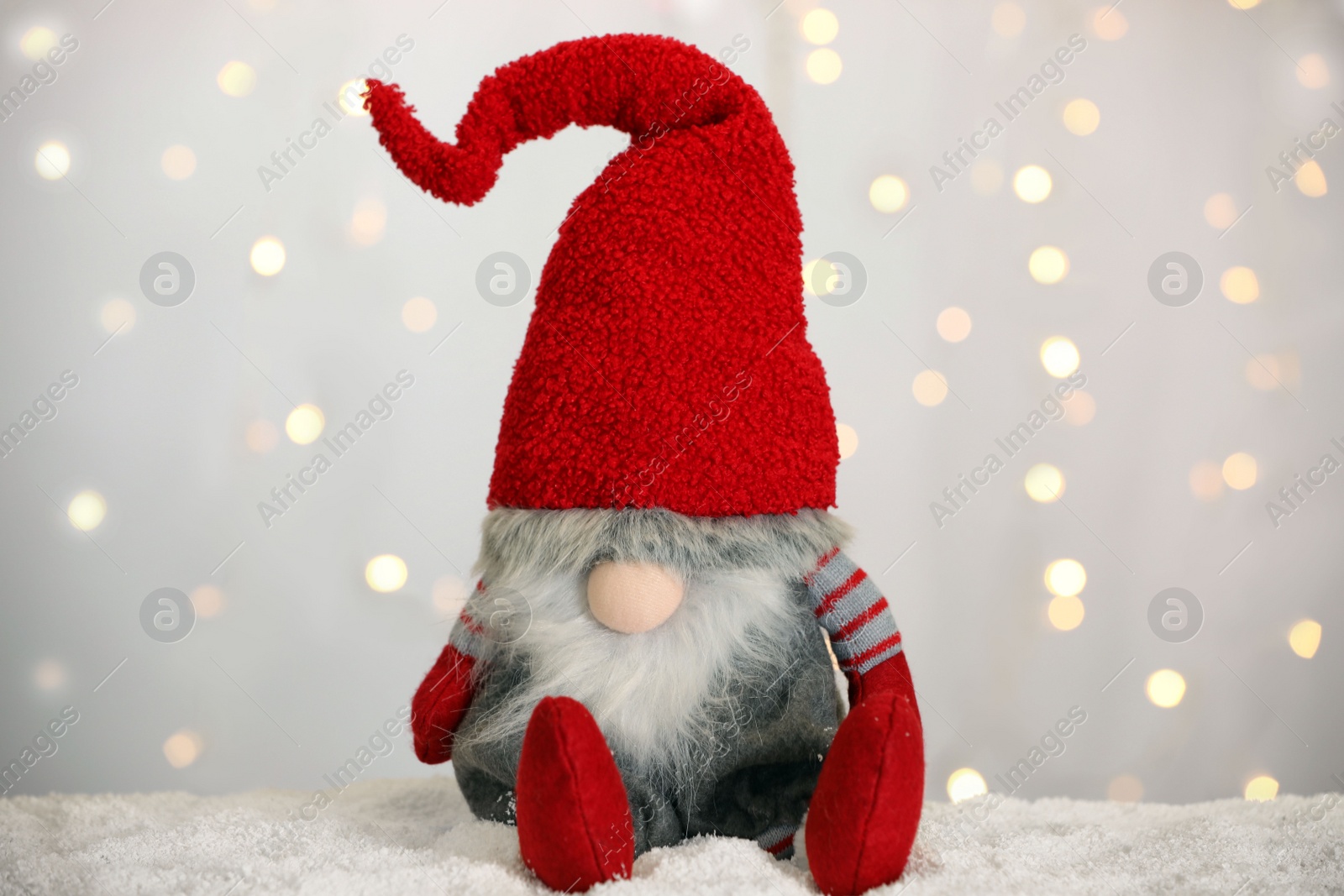 Photo of Cute Christmas gnome on snow against blurred festive lights