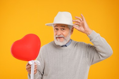 Photo of Senior man in hat with red heart shaped balloon on yellow background