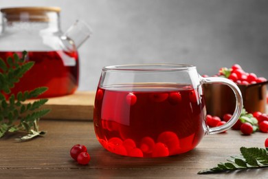 Photo of Tasty hot cranberry tea in glass and fresh berries on wooden table