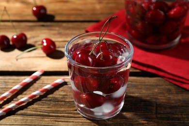 Photo of Sweet red cherries with ice cubes in glass on wooden table