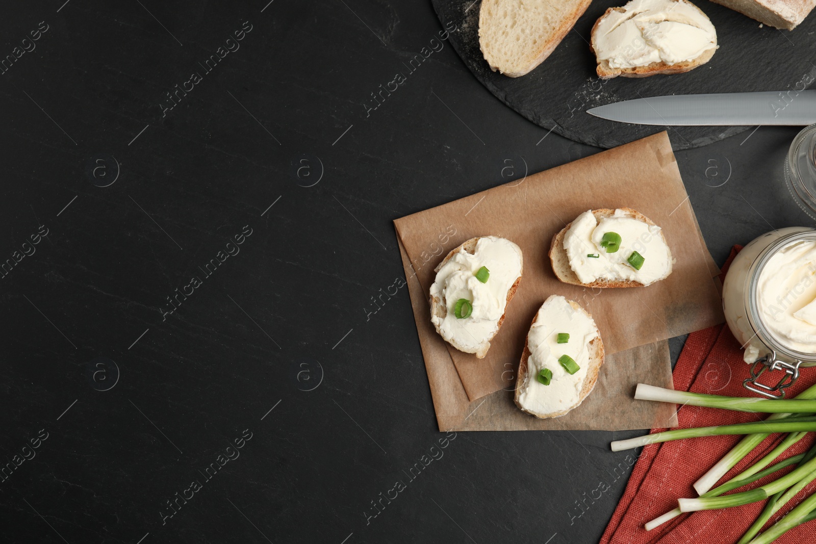 Photo of Bread with cream cheese and green onion on black table, flat lay. Space for text