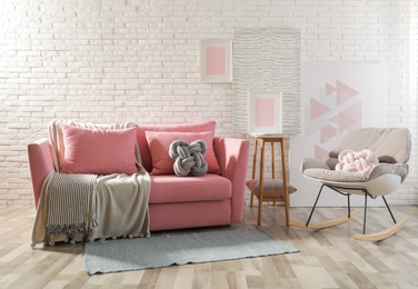 Photo of Stylish living room interior with sofa and rocking armchair near brick wall