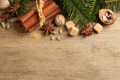 Photo of Different aromatic spices and fir branches on wooden table, flat lay. Space for text