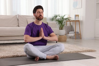 Photo of Man meditating on yoga mat at home. Harmony and zen