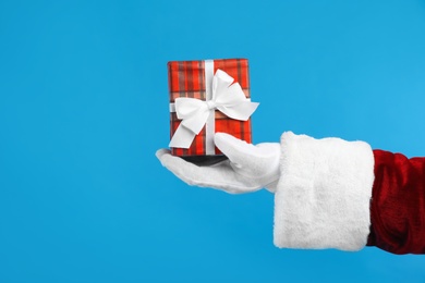 Santa Claus holding Christmas gift on blue background, closeup of hand
