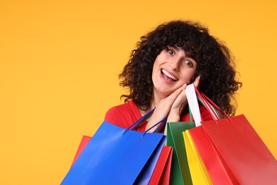 Happy young woman with shopping bags on yellow background