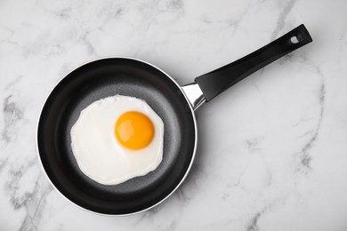 Tasty fried egg in pan on white marble table, top view