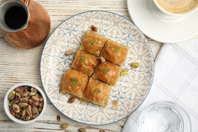 Delicious baklava with pistachios, nuts and hot coffee on white wooden table, flat lay