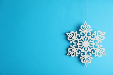 Photo of Beautiful decorative snowflake hanging on light blue background, space for text