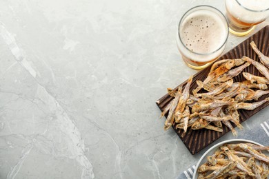 Delicious dried anchovies and glasses of beer on light grey marble table, flat lay. Space for text