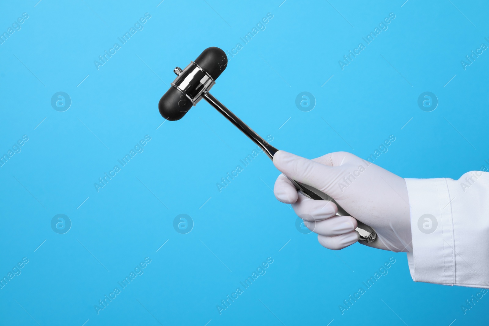 Photo of Doctor holding reflex hammer on light blue background, closeup. Nervous system diagnostic