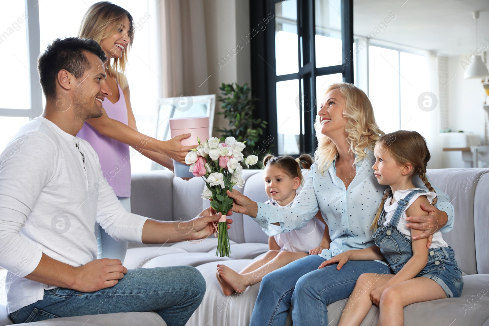 Photo of Happy family with little children congratulating mature woman in living room