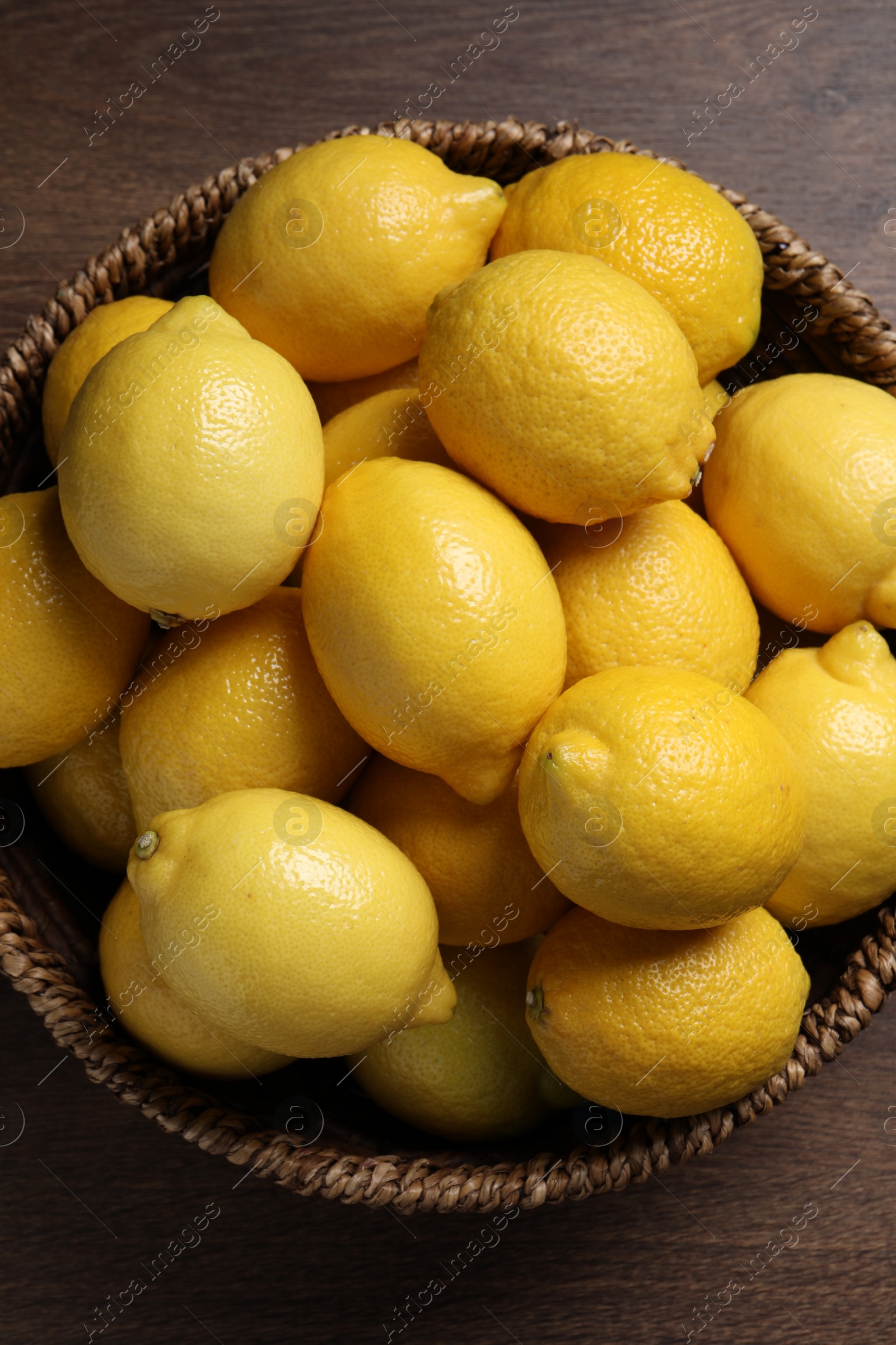 Photo of Fresh lemons in wicker basket on wooden table, top view