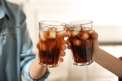 Photo of Women holding glasses of cola with ice on blurred background, closeup