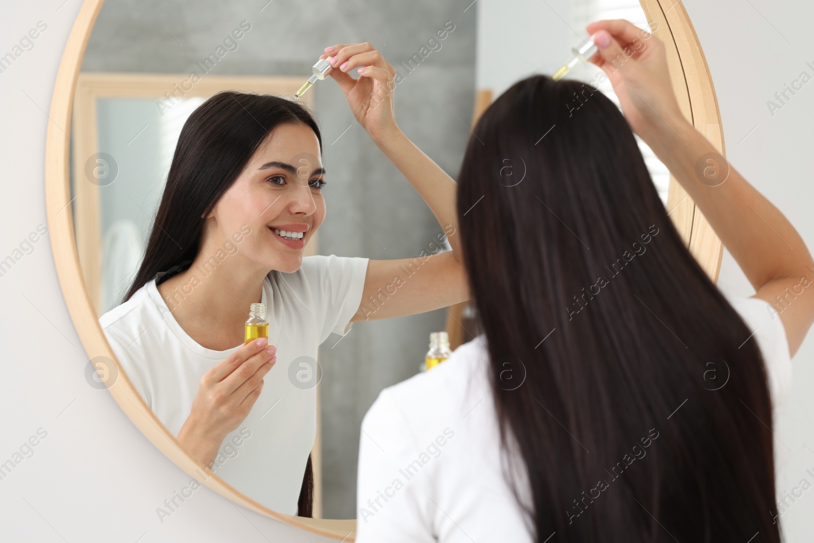 Photo of Beautiful woman applying hair serum in bathroom. Cosmetic product