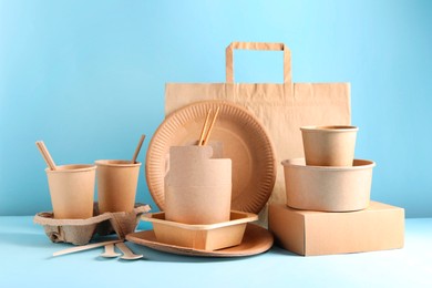 Photo of Eco friendly food packaging. Paper containers, tableware and bag on white table against light blue background