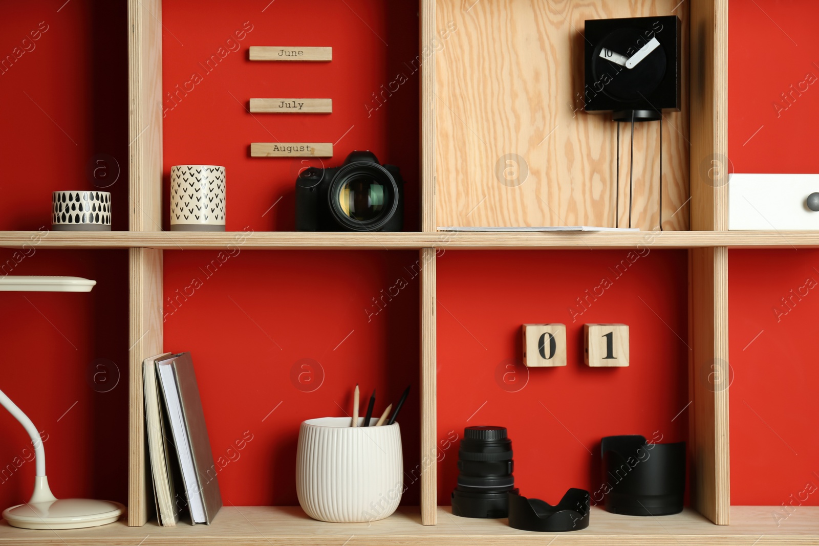 Photo of Stylish wooden shelves with photography equipment and decorative elements on red wall