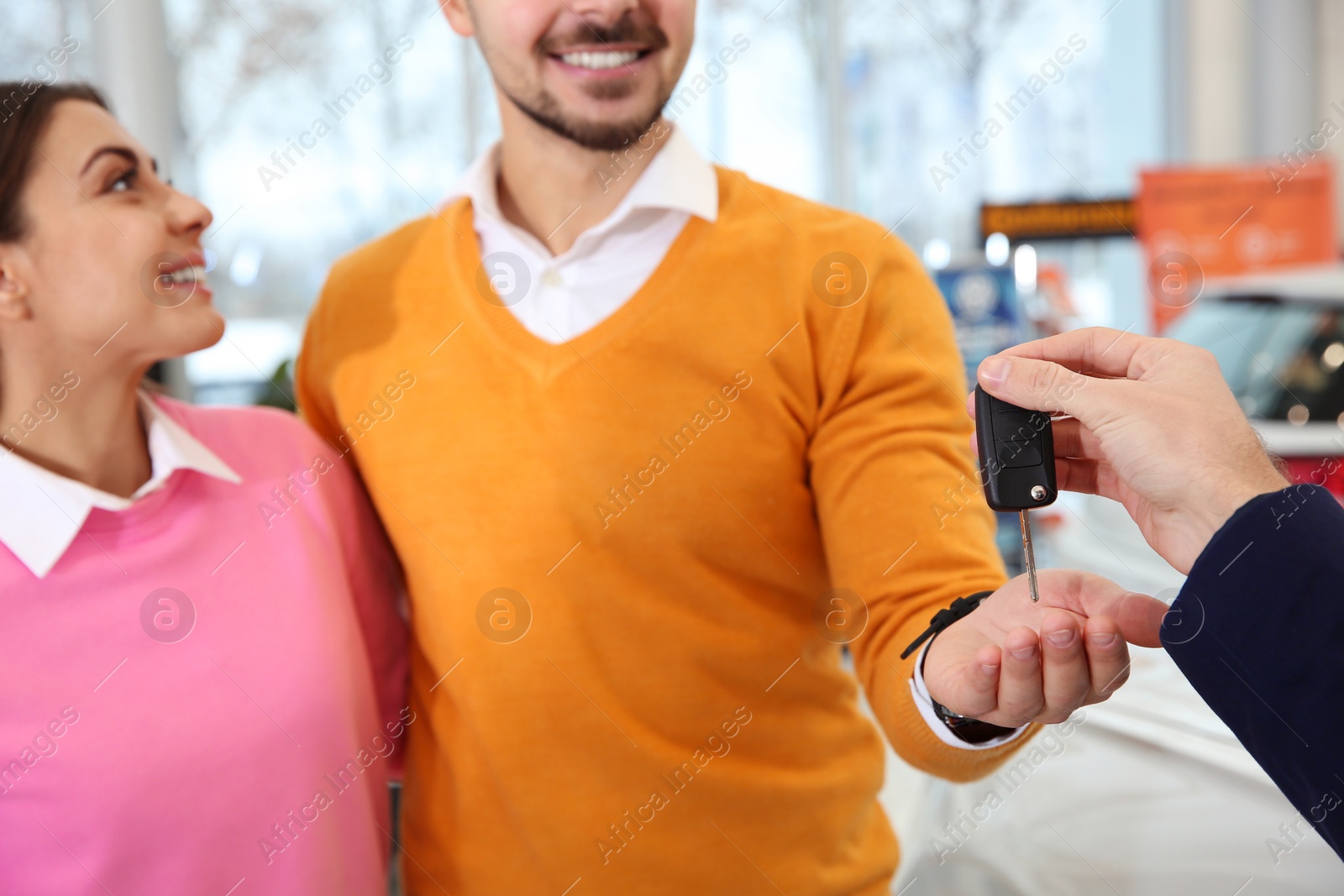 Photo of Car salesman giving key to couple in dealership, closeup