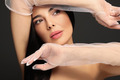 Photo of Portrait of young woman in elegant evening gloves on black background, closeup