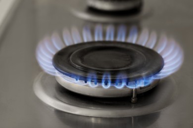 Photo of Gas burner with burning flame on cooktop, closeup