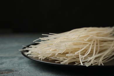 Plate with raw rice noodles on wooden table, closeup. Delicious pasta