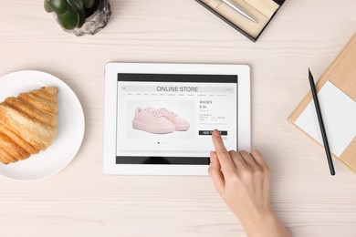 Woman with tablet shopping online at white wooden table, top view