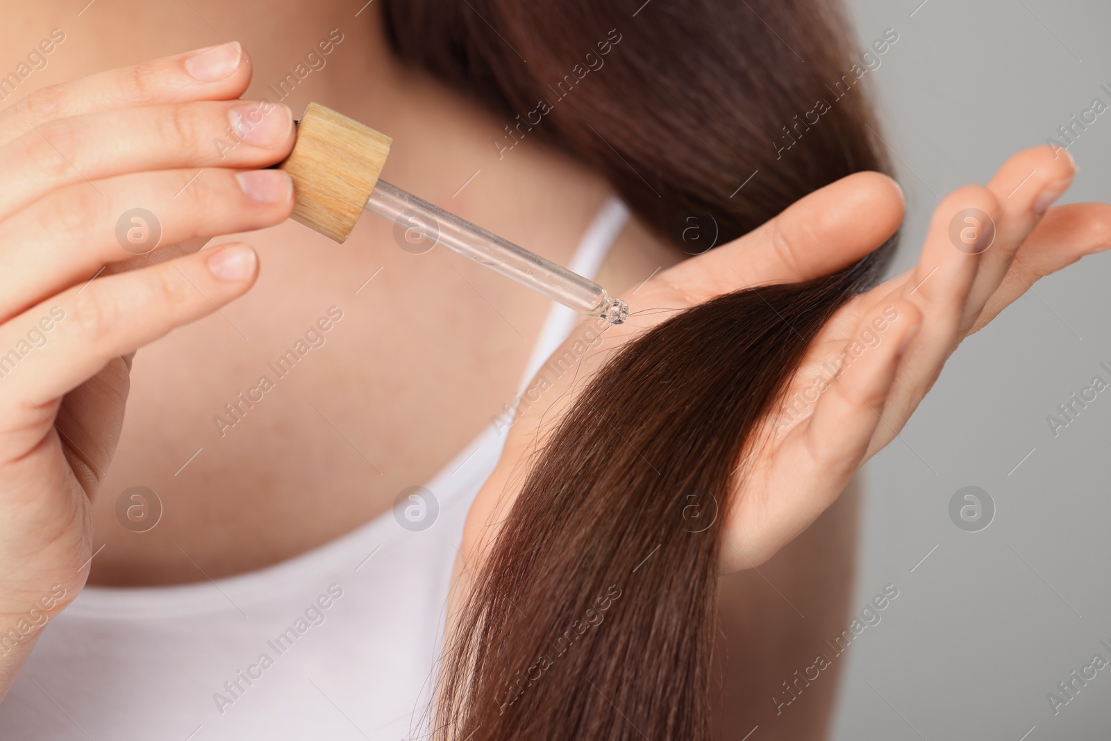 Photo of Woman applying essential oil onto hair on grey background, closeup