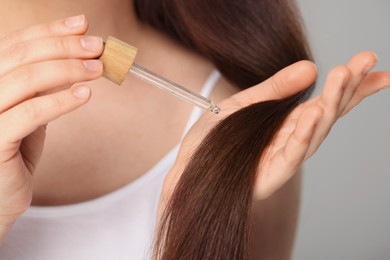 Woman applying essential oil onto hair on grey background, closeup