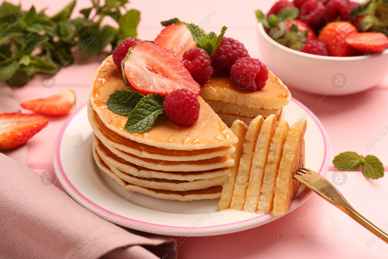 Photo of Eating delicious pancakes with fresh berries and honey at pink wooden table, closeup