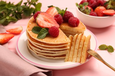 Eating delicious pancakes with fresh berries and honey at pink wooden table, closeup