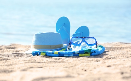 Photo of Bright towel, hat, flip flops and goggles on sand near sea. Beach object