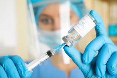 Doctor filling syringe with vaccine against Covid-19 in hospital, focus on hands