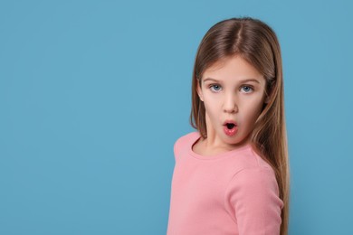 Photo of Portrait of surprised girl on light blue background. Space for text